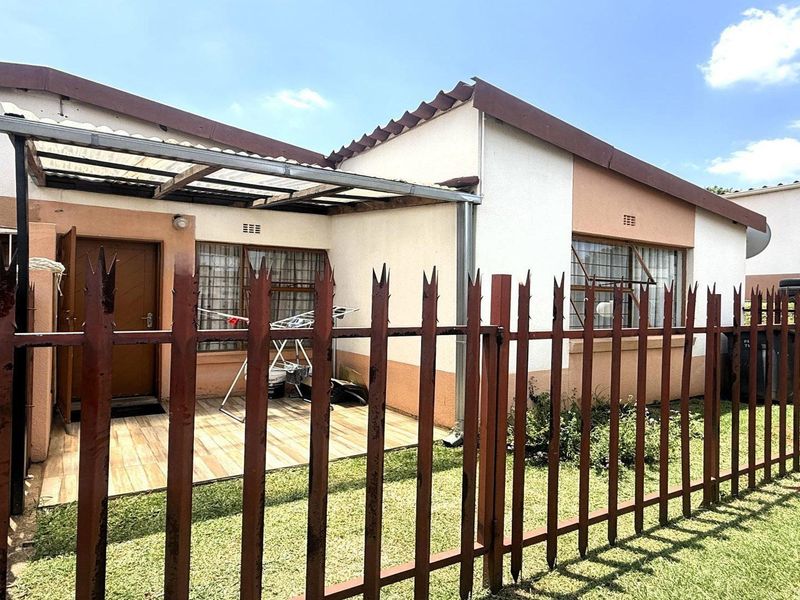 Front exterior view of the apartment featuring a small tiled patio, covered entrance area, and secure metal perimeter fencing.