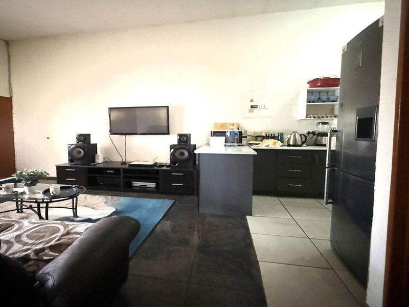 Open plan living area featuring a compact kitchen with dark cabinetry, a central island, and tiled flooring throughout the combined space.