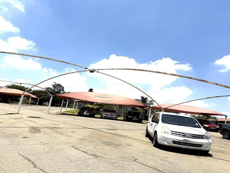 Outdoor parking area featuring multiple shade cloth carports with metal support structures and asphalt paving.