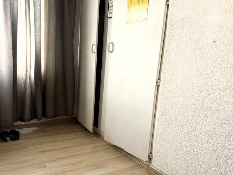 A bedroom interior featuring laminate flooring, textured walls, and a built-in wardrobe with visible wear on the door base.