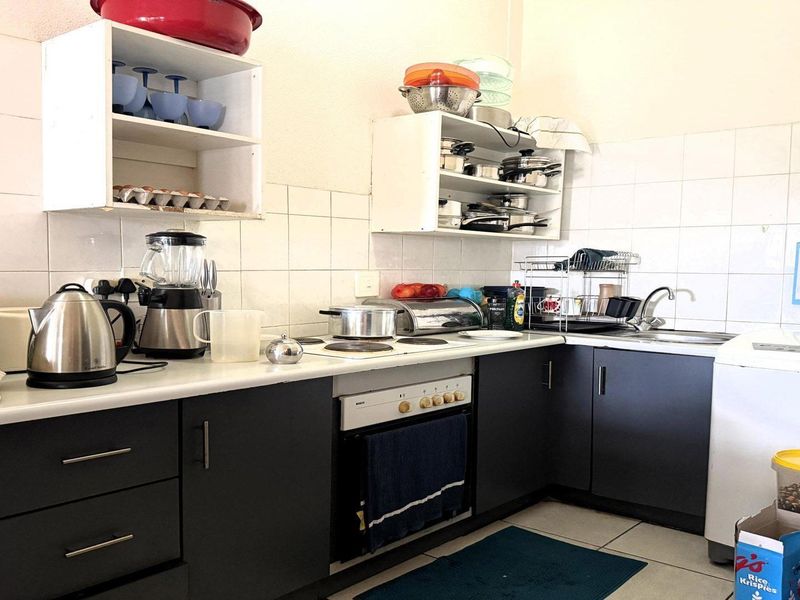 A functional kitchen featuring dark cabinetry, laminate countertops, an electric hob, built-in oven, and tiled splashback with ample storage space.