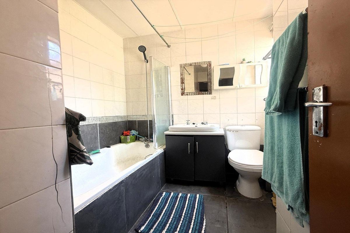 A functional bathroom featuring a bathtub with shower attachment, vanity basin, and toilet, finished with tiled walls and flooring.