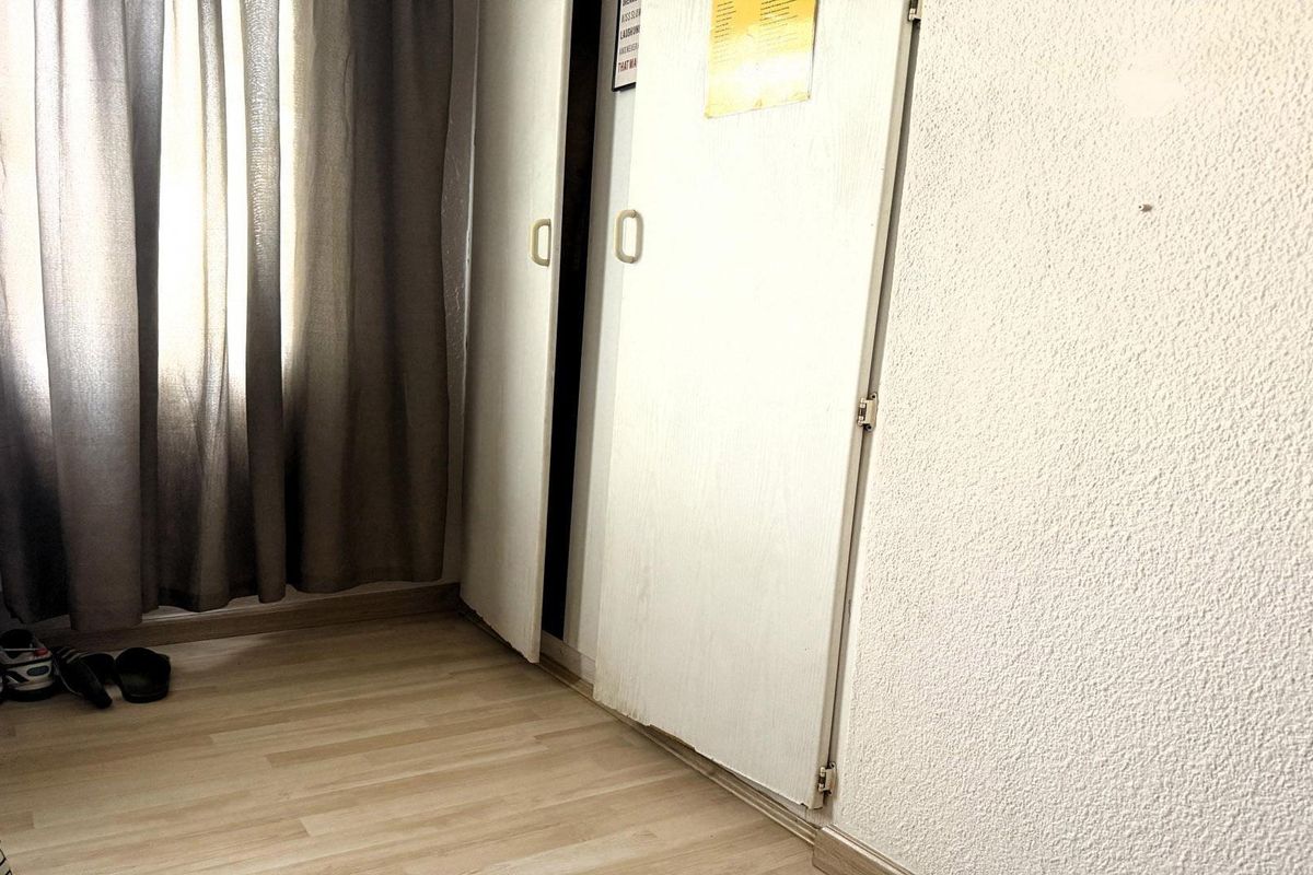 A bedroom interior featuring laminate flooring, textured walls, and a built-in wardrobe with visible wear on the door base.
