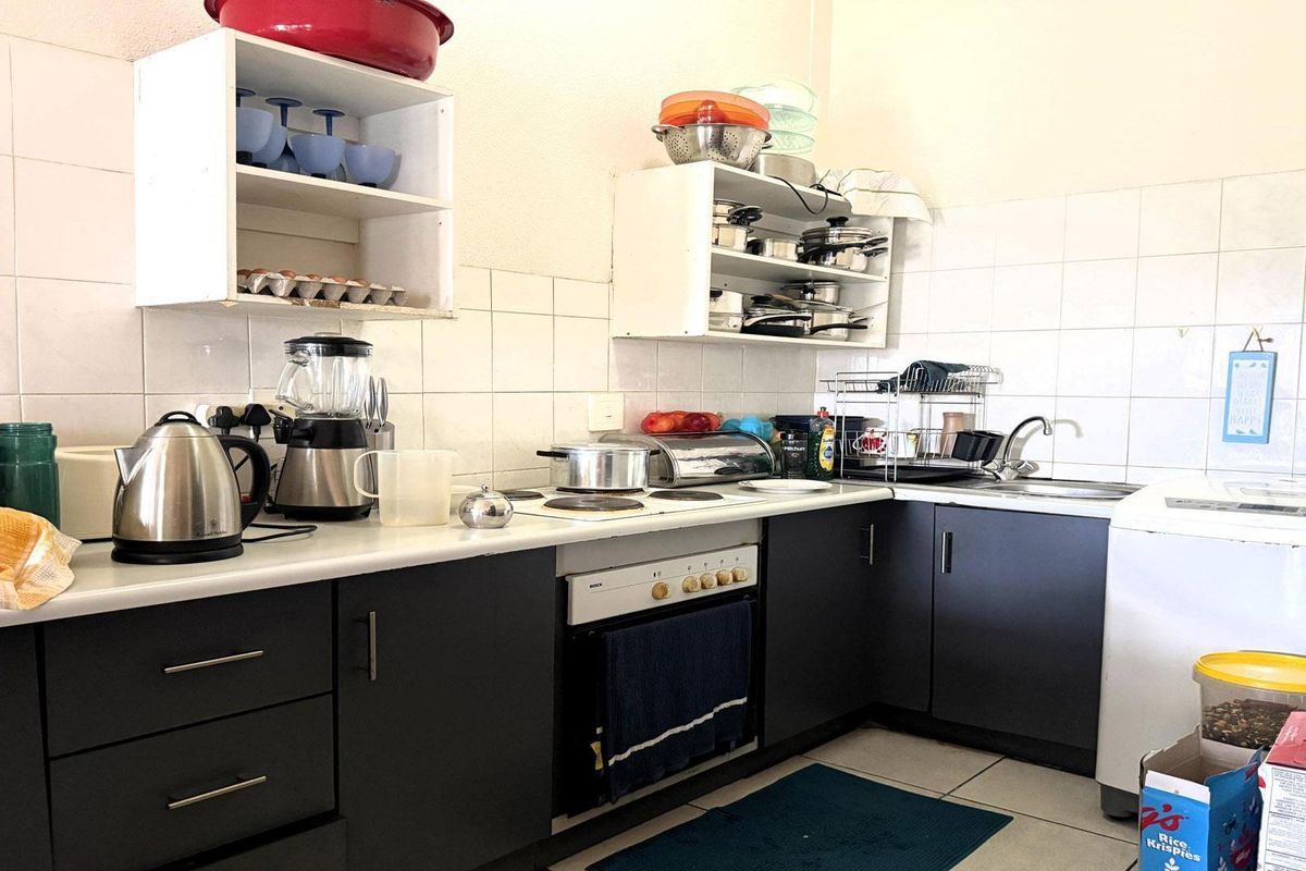 A functional kitchen featuring dark cabinetry, laminate countertops, an electric hob, built-in oven, and tiled splashback with ample storage space.