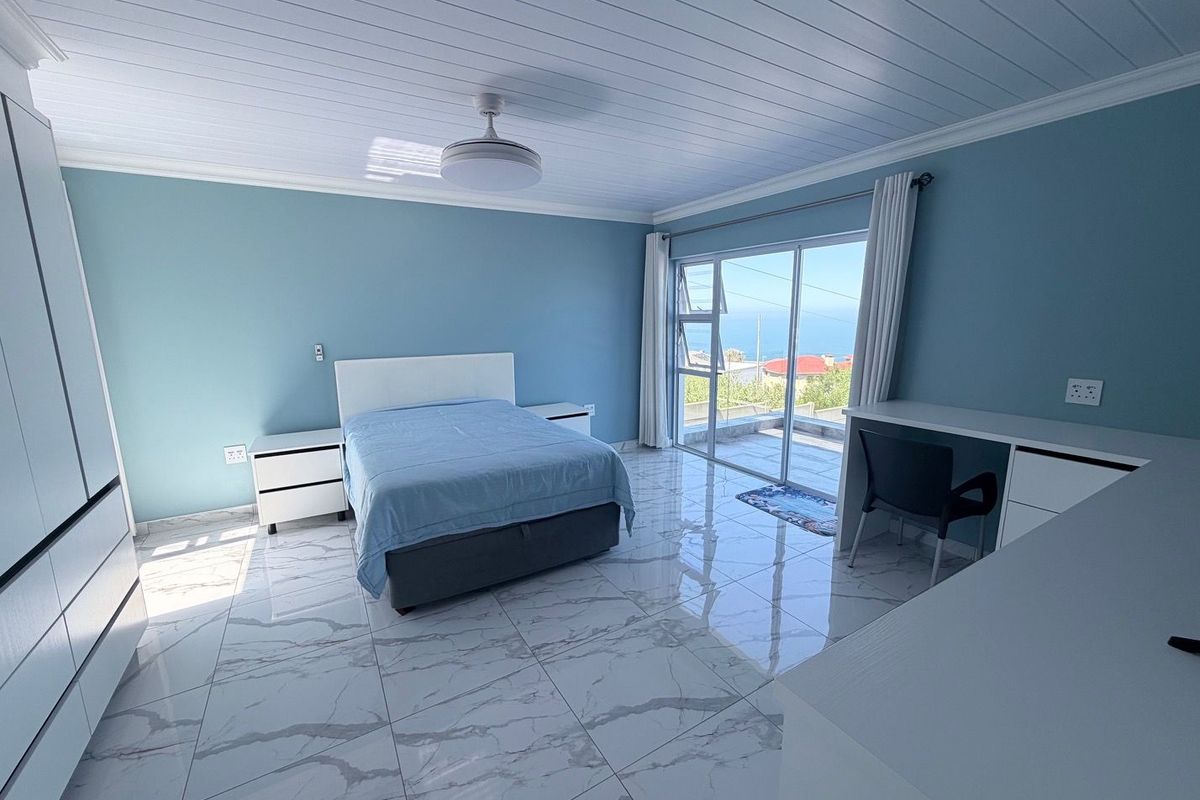 Spacious bedroom featuring modern marble-look floor tiles, built-in cabinetry, a ceiling fan, and sliding glass doors opening to a balcony with ocean views.