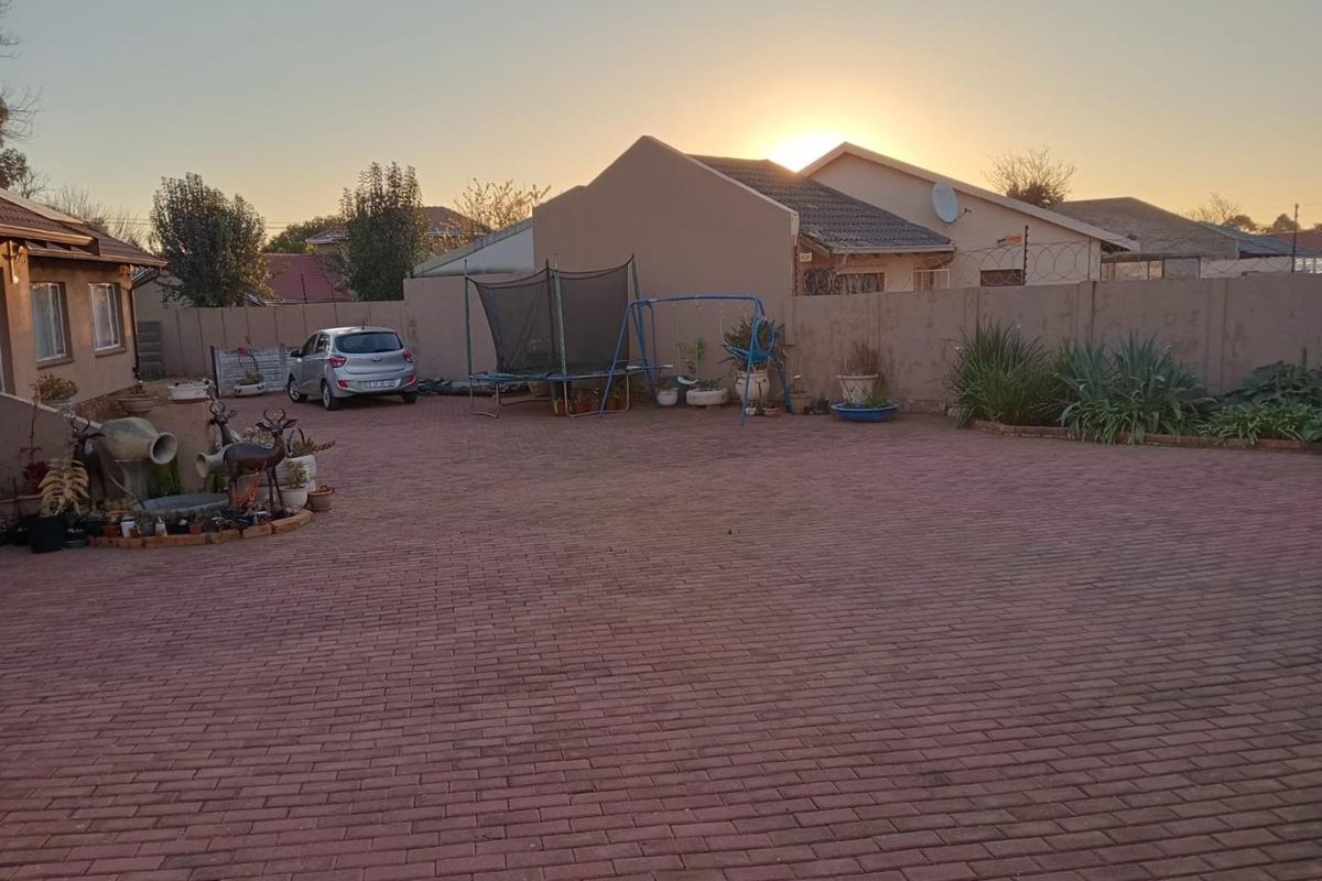 Spacious paved driveway and courtyard area featuring perimeter walling and established garden beds, providing ample off-street parking space.