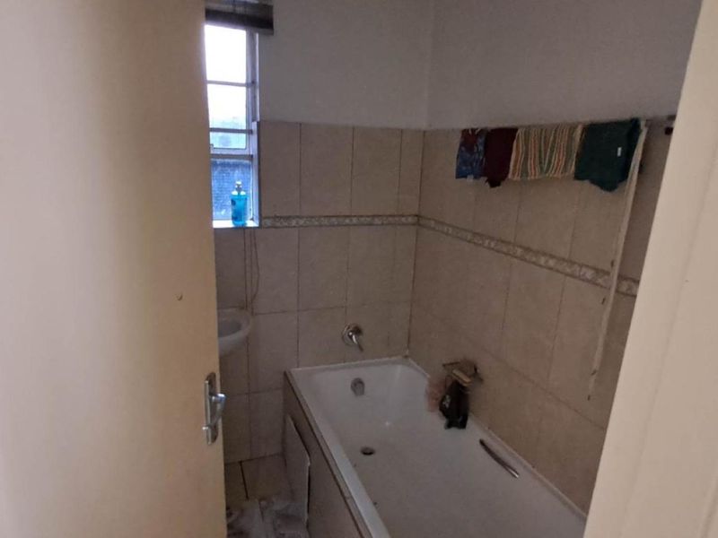 A compact bathroom featuring a standard bathtub, tiled walls, and floor, requiring some maintenance and cosmetic updates to improve its overall condition.