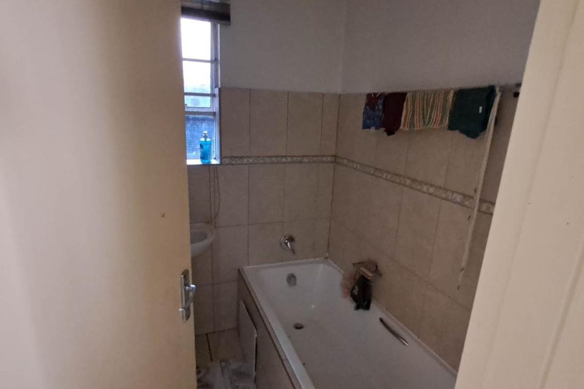 A compact bathroom featuring a standard bathtub, tiled walls, and floor, requiring some maintenance and cosmetic updates to improve its overall condition.
