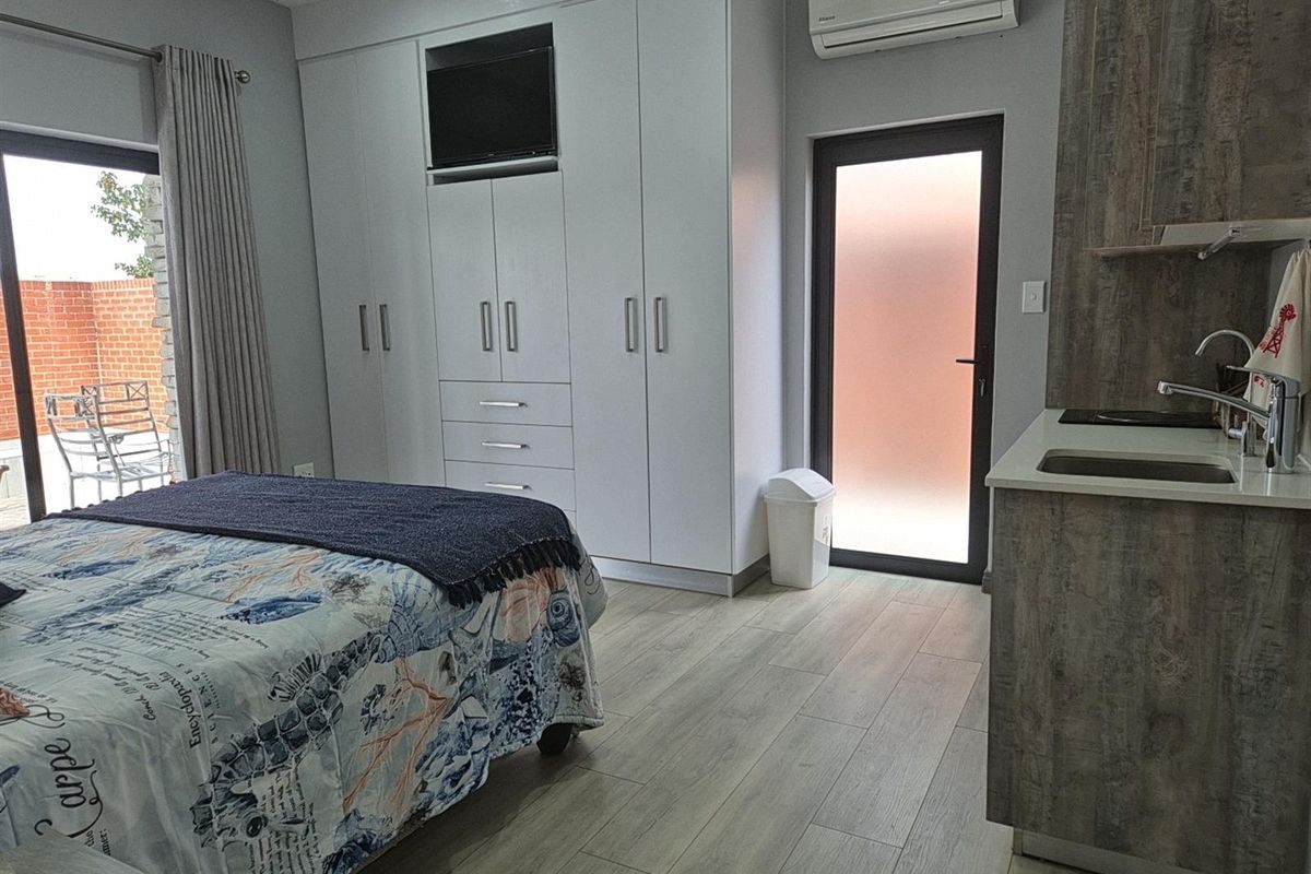 A modern studio bedroom featuring built-in wardrobes, a compact kitchenette with sink, and direct access to an outdoor patio area.