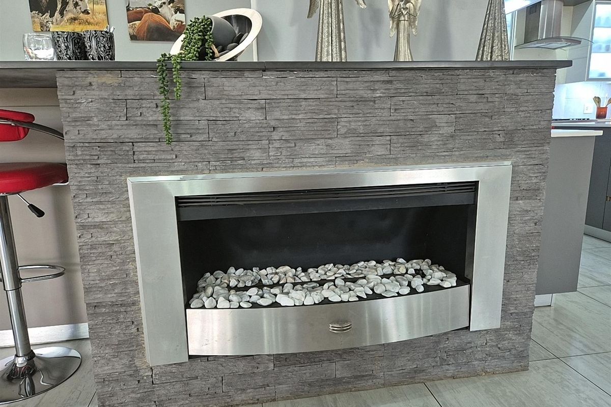 A modern fireplace feature wall finished in grey stacked stone with a stainless steel insert and decorative pebble bed.