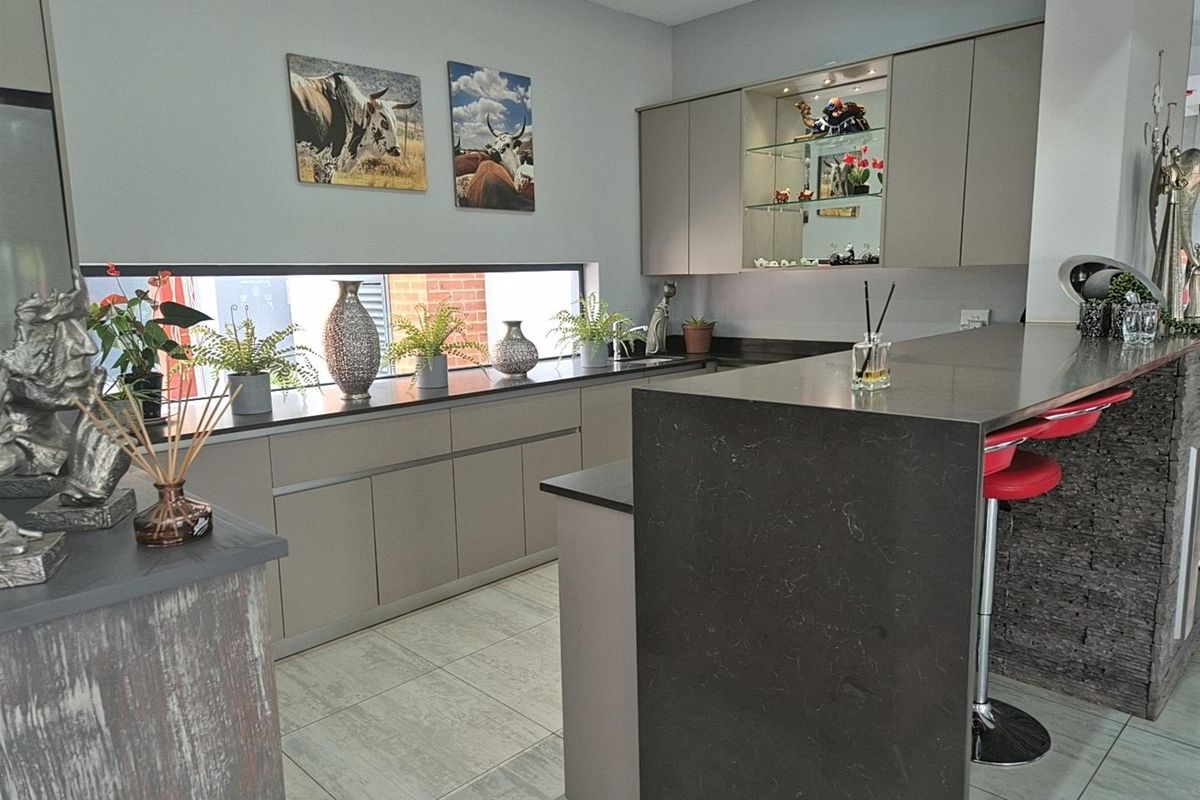 Modern kitchen featuring sleek cabinetry, stone countertops, a breakfast bar with stone cladding, and a horizontal window providing natural light.