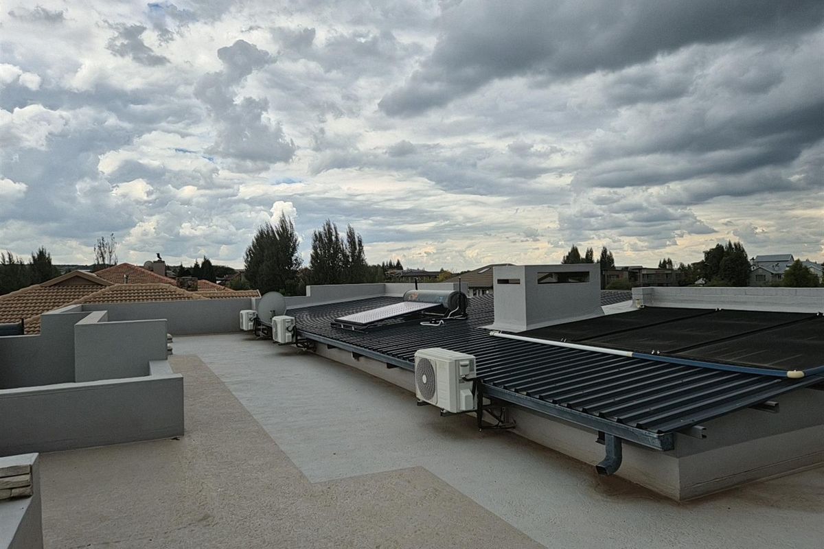 An elevated view of the property roof featuring solar water heating panels, air conditioning units, and a chimney stack.