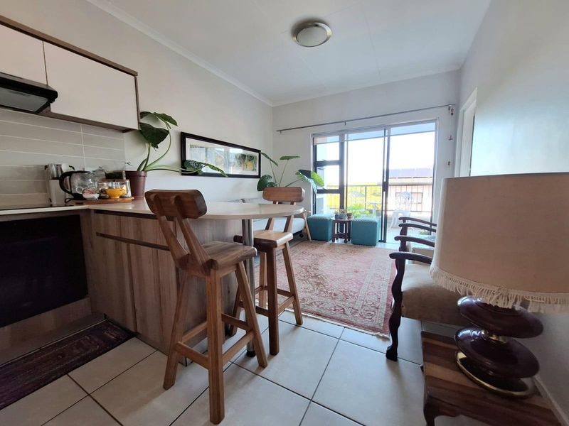 Open-plan living area featuring a compact kitchen with built-in cabinetry, breakfast bar, and direct access to a balcony through sliding glass doors.
