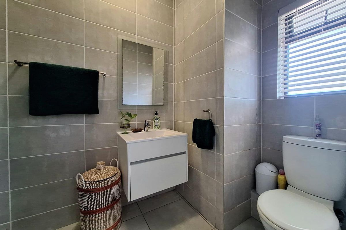 A modern, fully tiled bathroom featuring a wall-mounted vanity, a sleek basin with mixer tap, and a toilet, finished with neutral grey ceramic tiling.