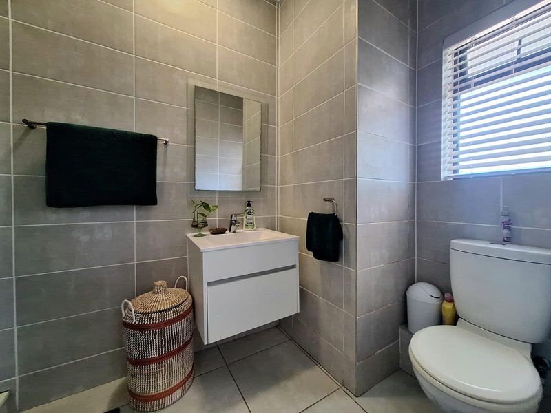 A modern, fully tiled bathroom featuring a wall-mounted vanity, a sleek basin with mixer tap, and a toilet, finished with neutral grey ceramic tiling.