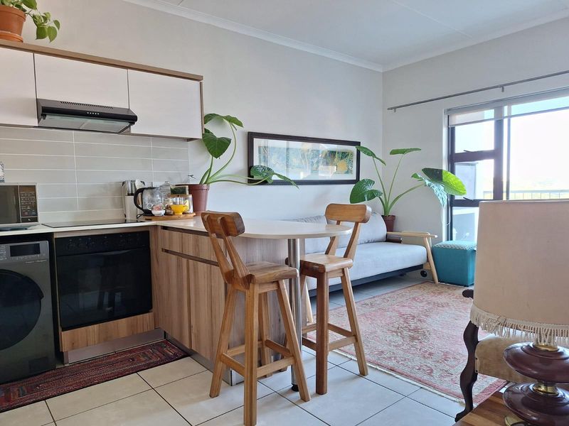 An open-plan living area featuring a modern kitchen with built-in cabinetry, oven, hob, and a breakfast bar, seamlessly connected to the living space.