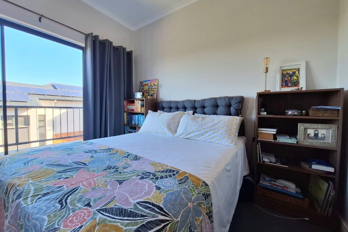 A well-lit bedroom featuring a sliding glass door that opens onto a private balcony with a metal railing.