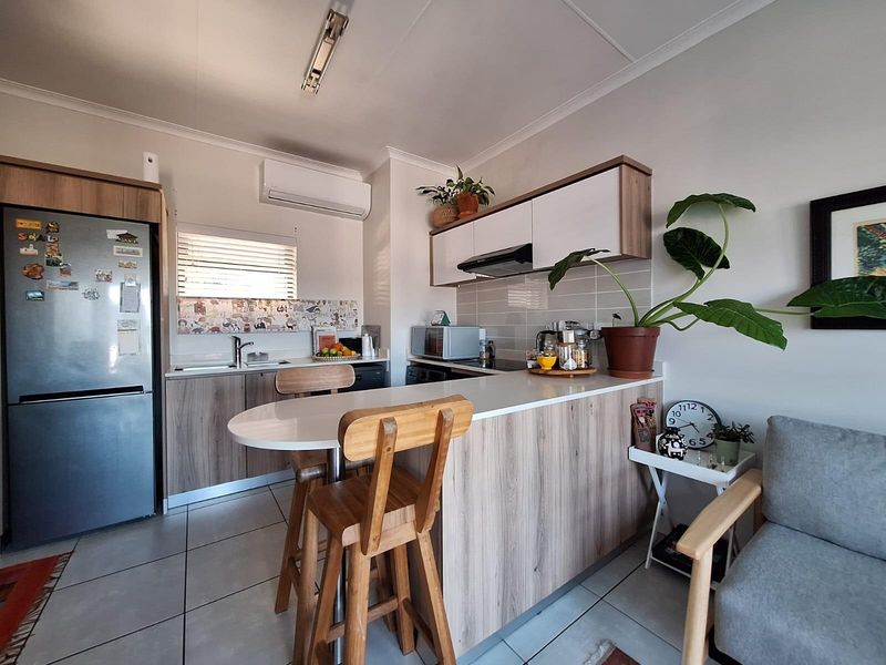 Modern open-plan kitchen featuring wood-finish cabinetry, a breakfast bar, tiled flooring, and an integrated air conditioning unit, creating a functional and cohesive living space.