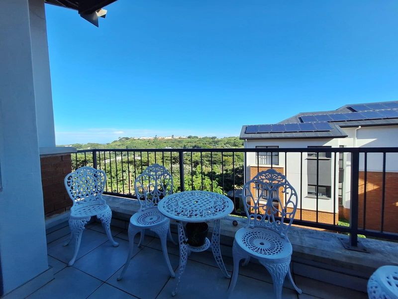 A covered balcony featuring tiled flooring and a metal balustrade, offering elevated views of the surrounding landscape and neighboring residential buildings.