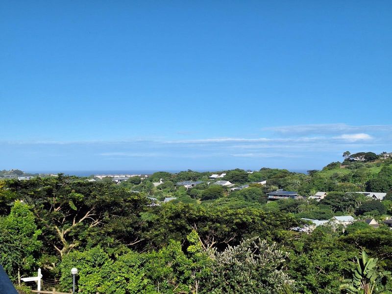 An elevated scenic view overlooking a lush green landscape with distant residential properties and a clear blue sky.