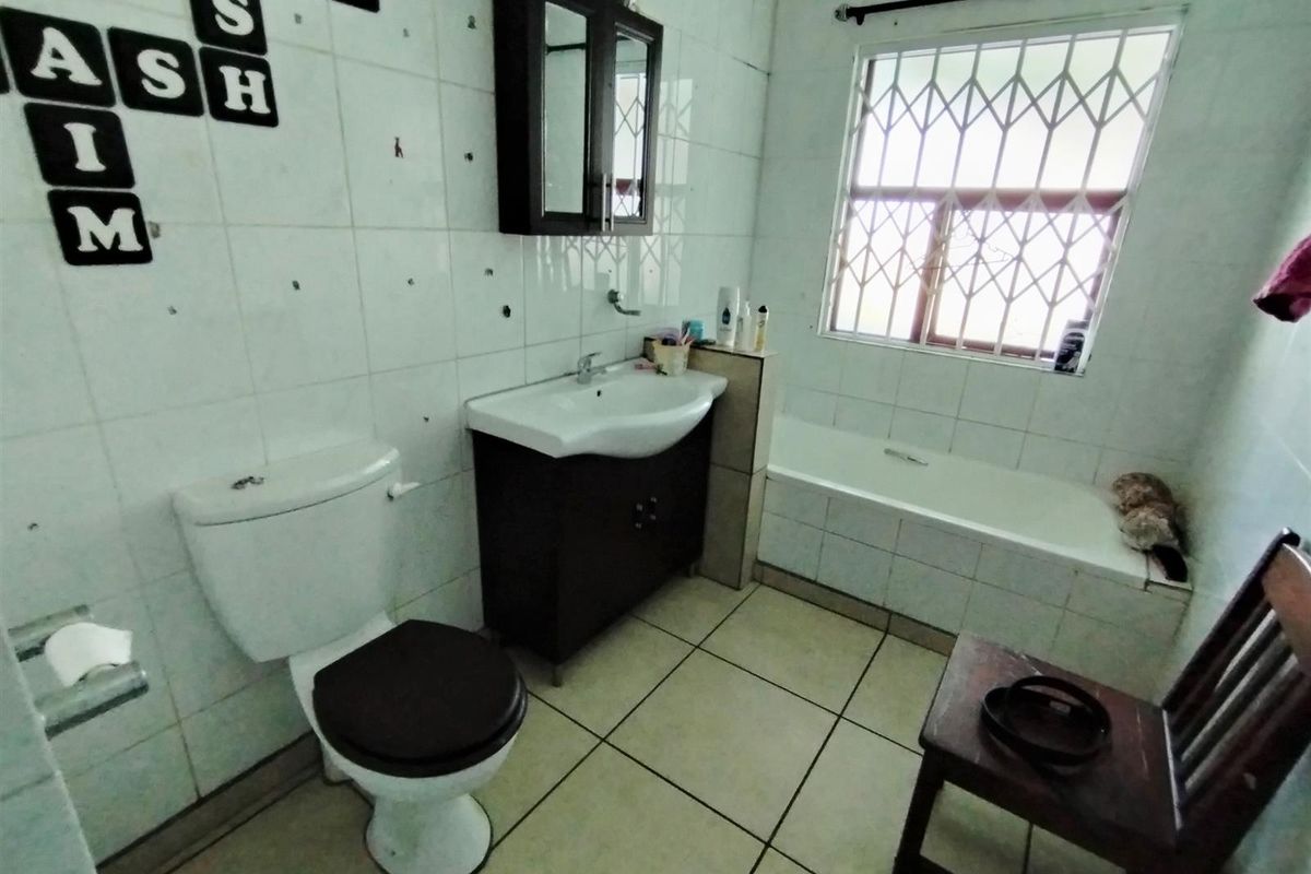A functional bathroom featuring a vanity, bathtub, and toilet, with tiled finishes. The walls require repair due to multiple holes from previous fixtures.