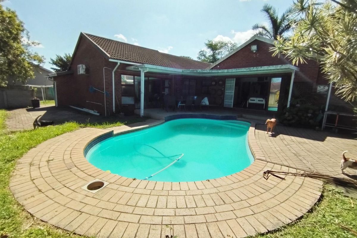 Rear exterior view featuring a swimming pool with brick paving and a covered patio area attached to the brick house.