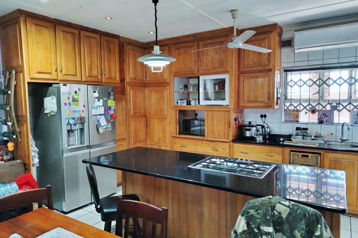 A functional kitchen featuring extensive wooden cabinetry, black granite countertops, a central island with a gas hob, and integrated appliances.