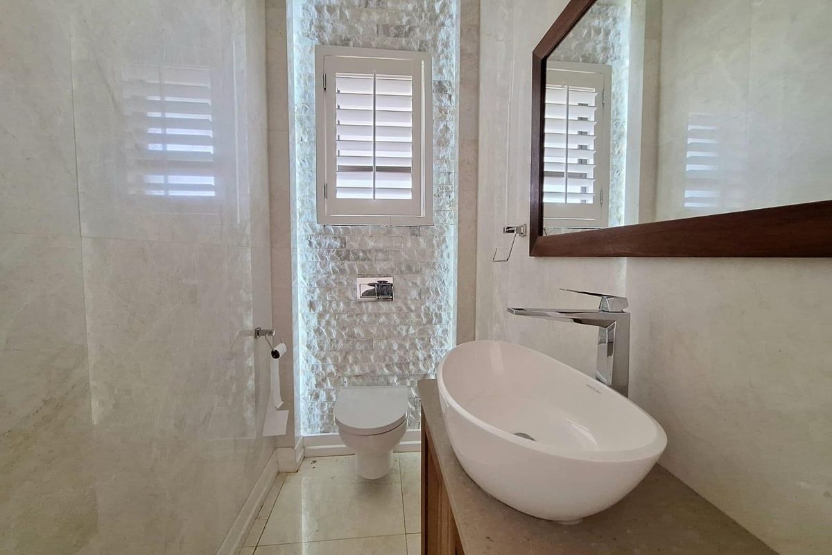 Modern bathroom featuring a stone-clad feature wall, wall-mounted toilet, vessel sink on a vanity, and plantation shutters.