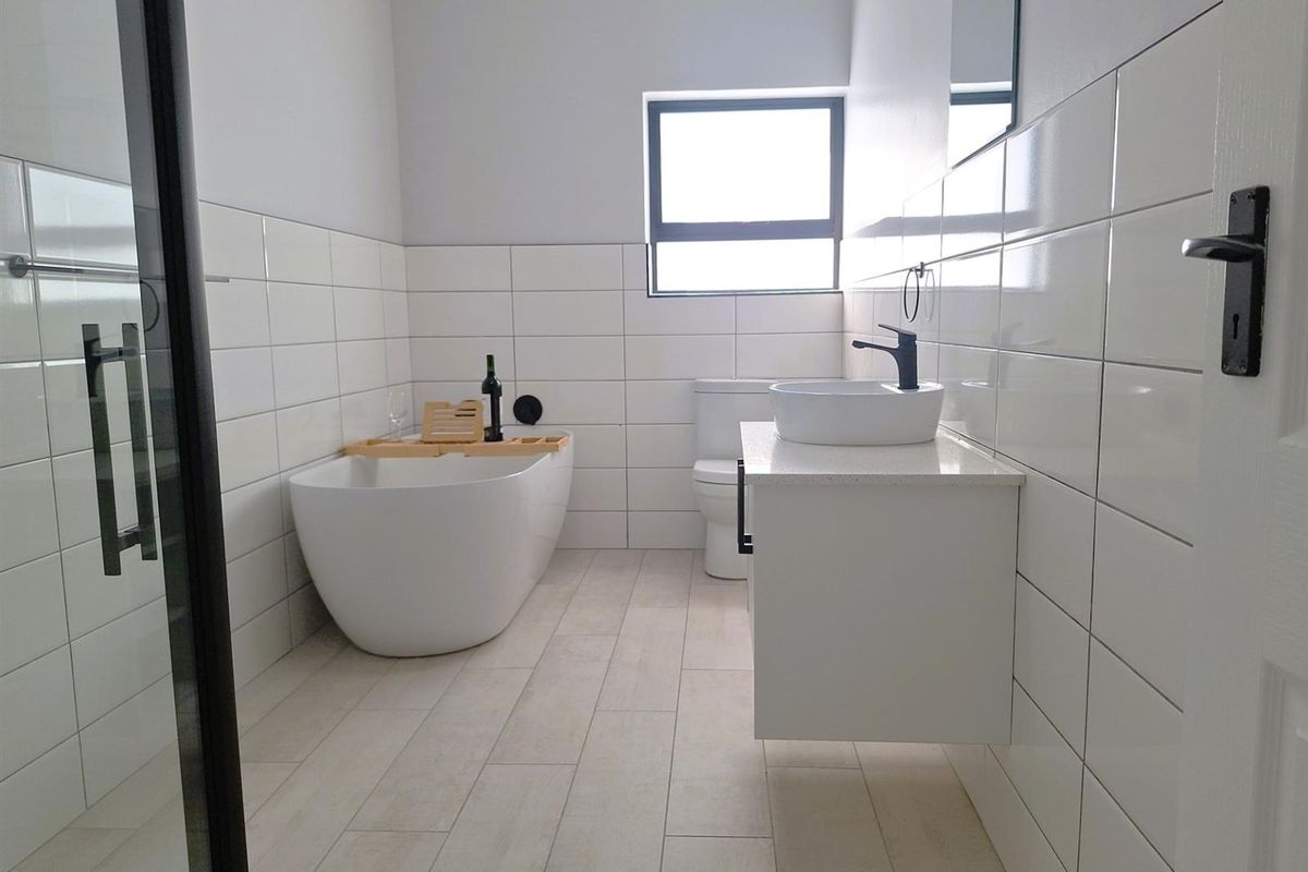 Modern bathroom featuring a freestanding bathtub, wall-mounted vanity with vessel sink, matte black fixtures, and floor-to-ceiling white subway tiling.