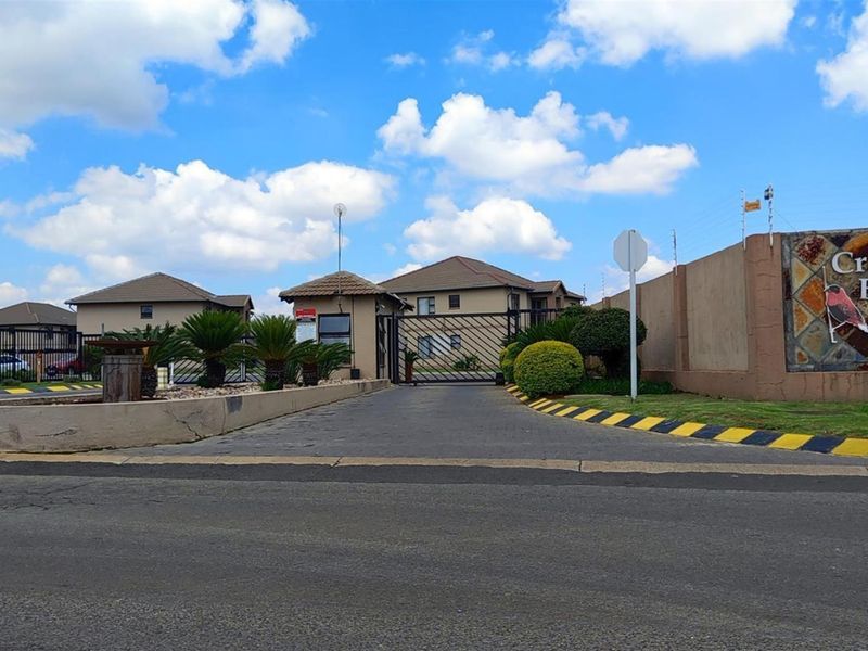 The main entrance to Crown Bishop complex, featuring a secure gated access point, guard house, perimeter wall with electric fencing, and paved driveway.