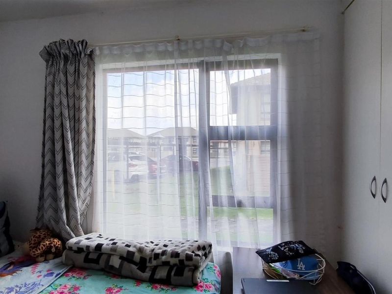 A bedroom featuring a built-in wardrobe and a large window with natural light, providing a view of the surrounding apartment complex.