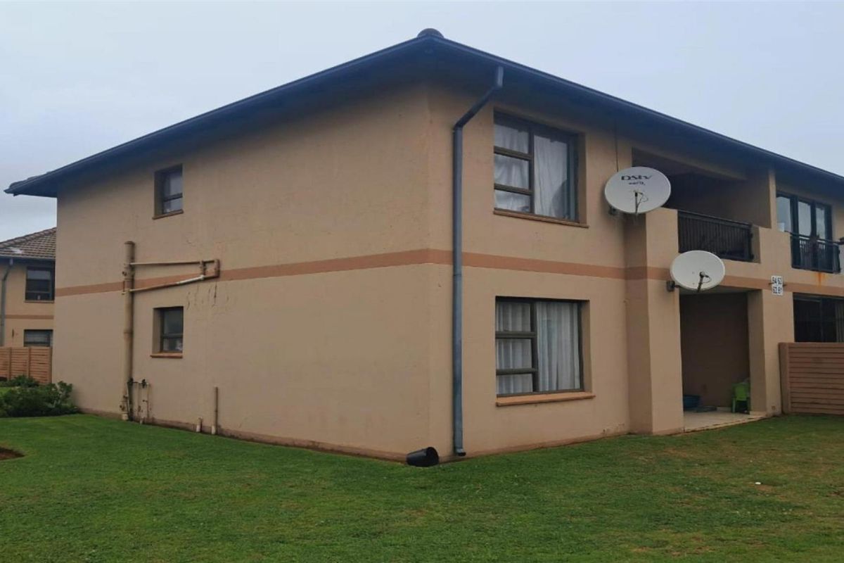 Exterior view of a two-story apartment building featuring a rear balcony, satellite dishes, and surrounding lawn area.