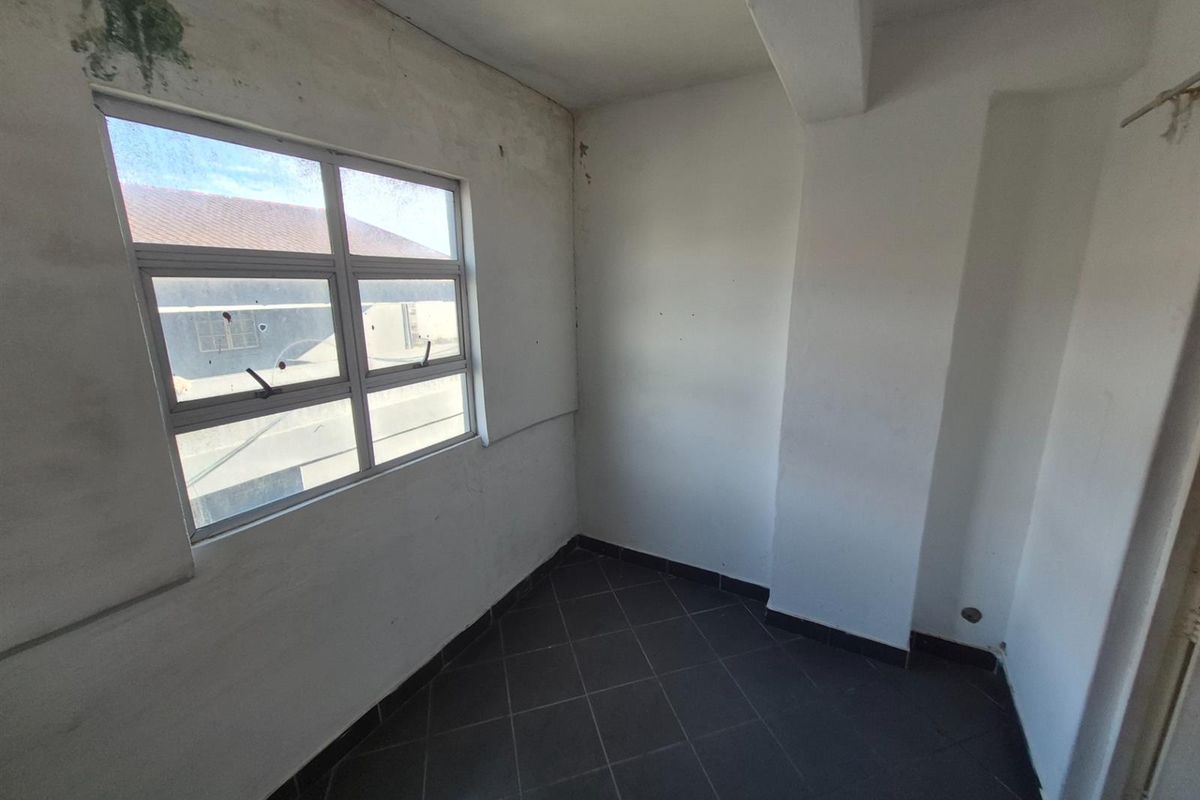 An empty bedroom featuring dark tiled flooring and an aluminium window, currently requiring cosmetic attention and wall repairs.