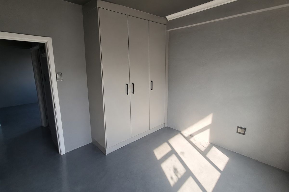 A clean, empty bedroom featuring neutral grey walls, smooth flooring, and a modern built-in wardrobe with matte finish doors.