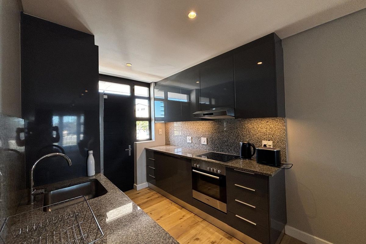 Modern kitchen featuring high-gloss cabinetry, granite countertops, integrated oven and hob, and timber flooring with recessed lighting.