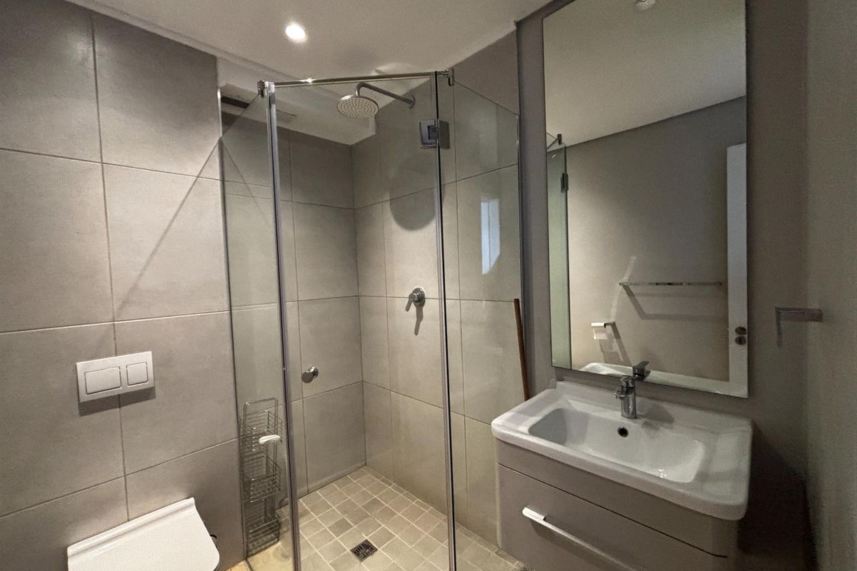 Modern bathroom featuring a glass-enclosed shower, wall-mounted toilet, and a sleek vanity cabinet with a large mirror.