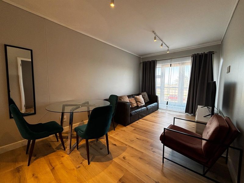 A well-maintained living room featuring modern laminate flooring, recessed and track lighting, and a sliding glass door providing natural light.
