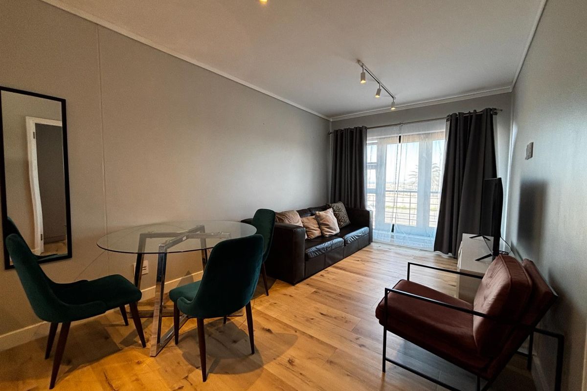 A well-lit living and dining area featuring timber flooring, modern track lighting, and direct access to a balcony through sliding glass doors.