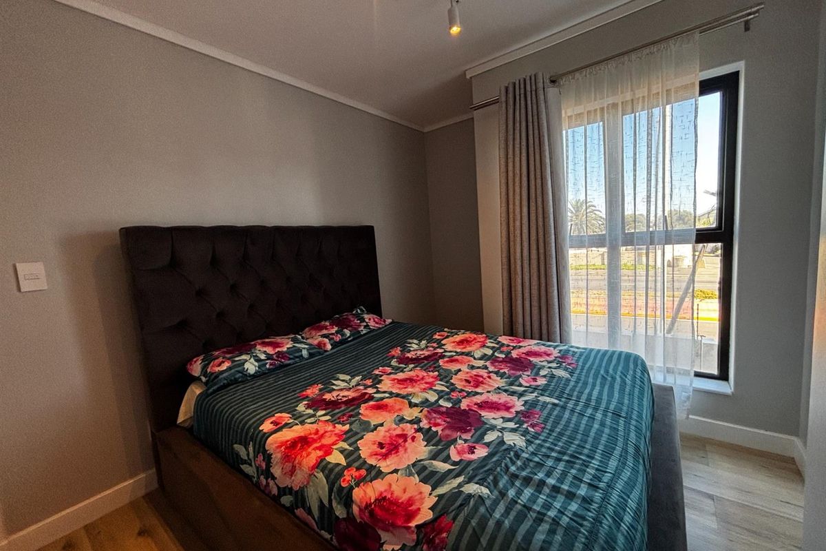 A well-maintained bedroom featuring modern laminate flooring, neutral wall finishes, and a large window with installed curtain rails for natural light.