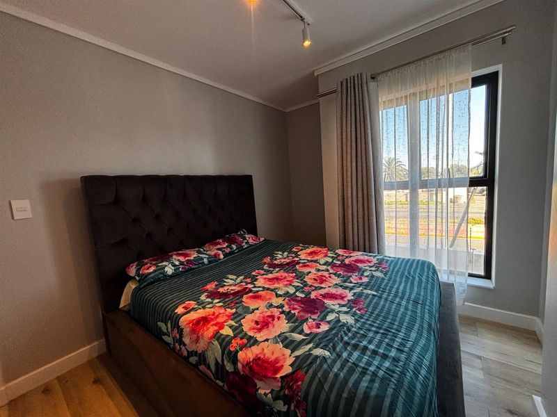 A well-maintained bedroom featuring modern laminate flooring, neutral wall finishes, and a large window with installed curtain rails for natural light.