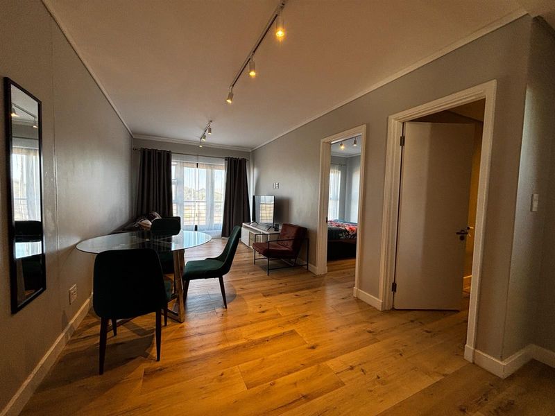 Open-plan living area featuring warm-toned laminate timber flooring, modern track lighting, and direct access to a balcony through sliding glass doors.