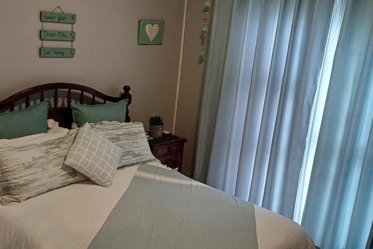 A cozy bedroom featuring neutral wall tones, a large window with floor-to-ceiling curtains, and space for a double bed.