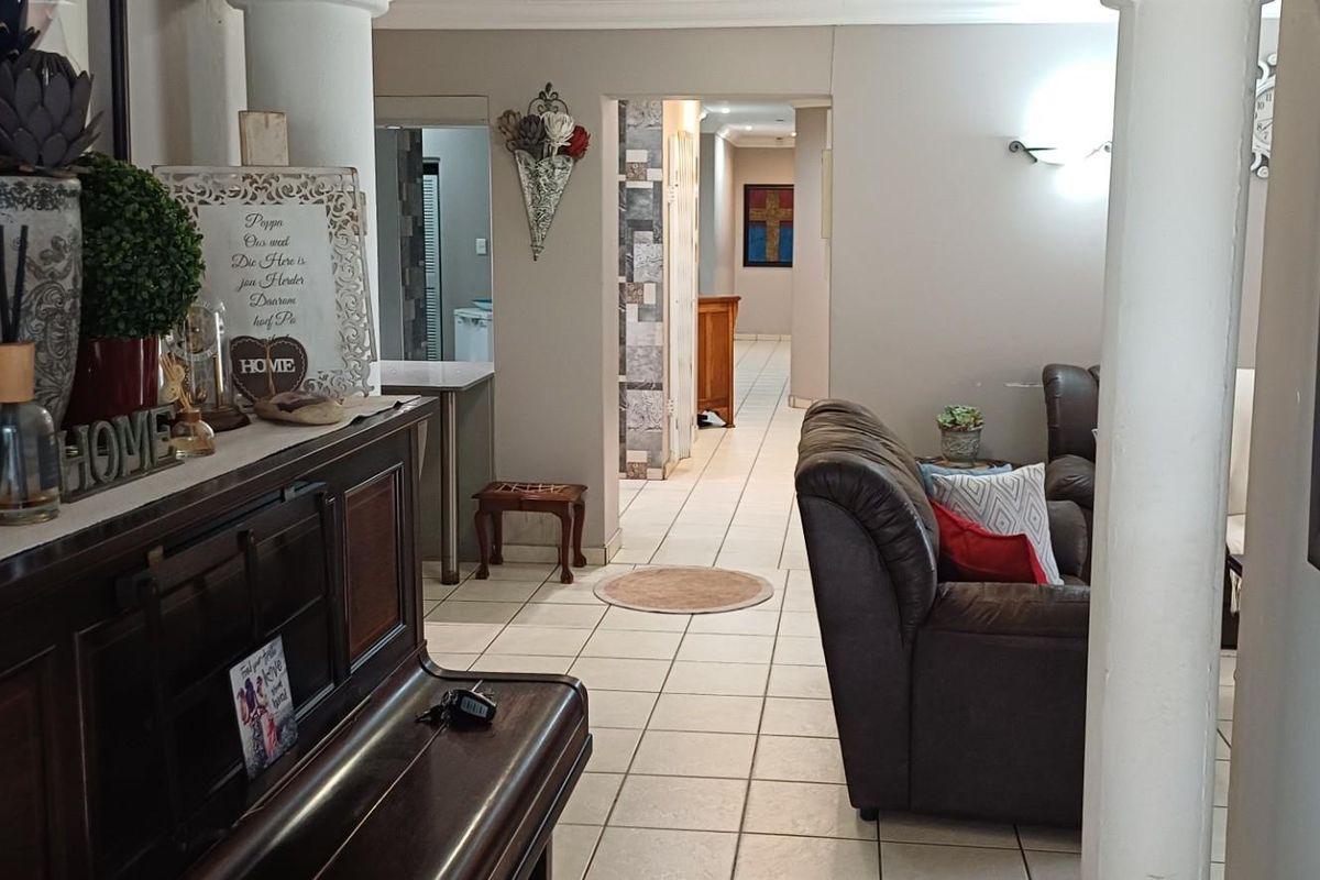 An interior view of a living area featuring tiled flooring, decorative columns, and a transition space leading to a hallway and secondary rooms.