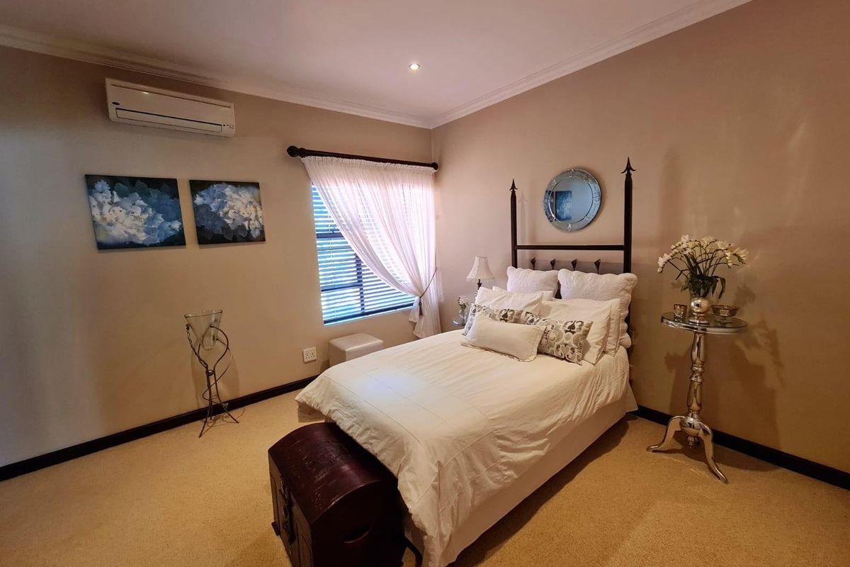 A well-maintained bedroom featuring neutral wall tones, carpeted flooring, recessed downlighting, and a wall-mounted air conditioning unit.