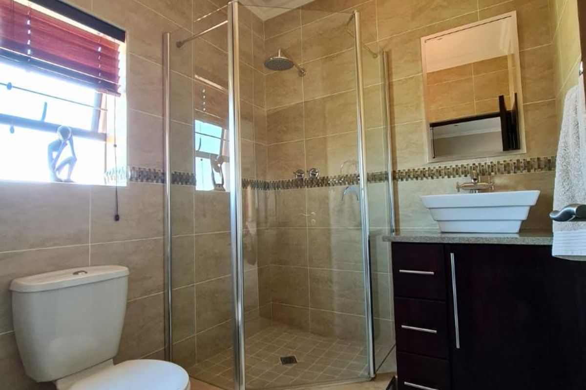 A well-maintained bathroom featuring a corner glass shower enclosure, a modern vessel sink vanity, and neutral wall tiling.