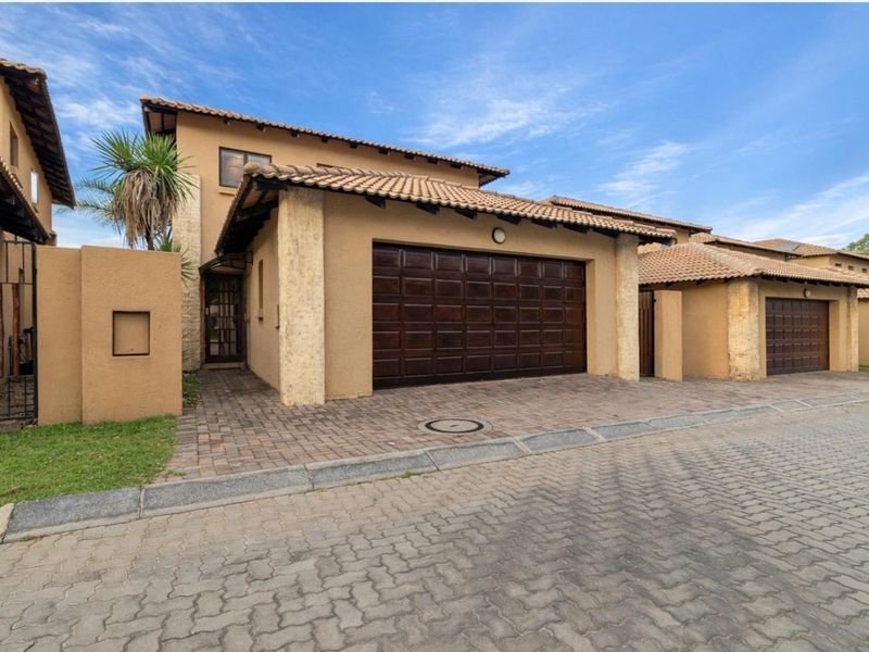 Exterior view of a townhouse featuring a double garage, paved driveway, and tiled roof architecture.