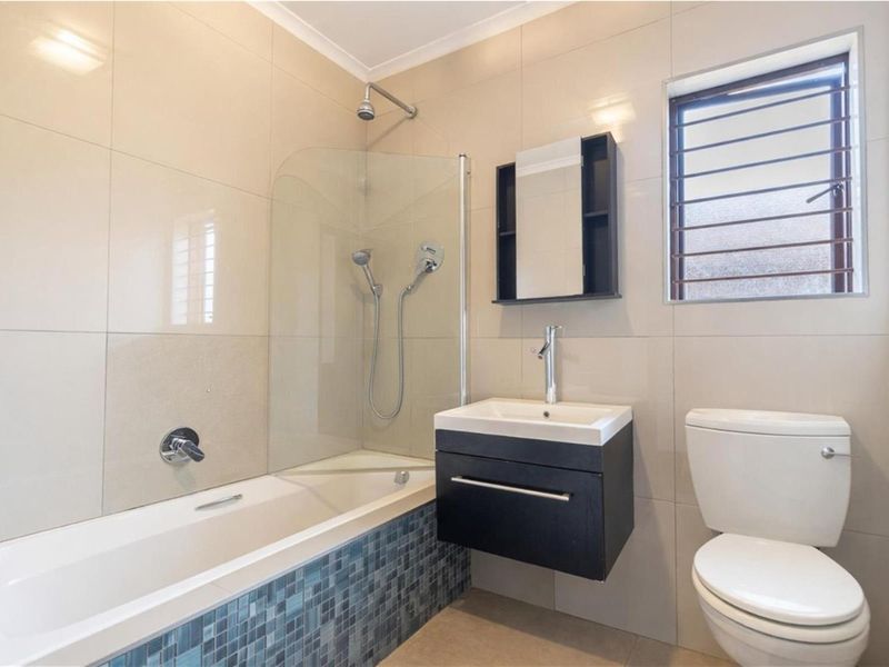 Modern bathroom featuring a wall-mounted vanity, a bathtub with a glass shower screen, and neutral wall tiling with a decorative mosaic accent.