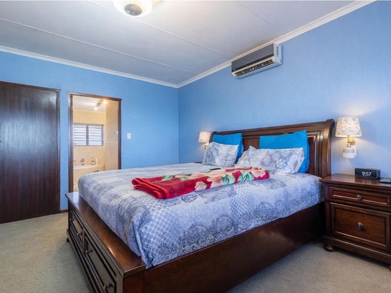 A bedroom featuring blue walls, carpeted flooring, a wall-mounted air conditioning unit, and an en-suite bathroom access.