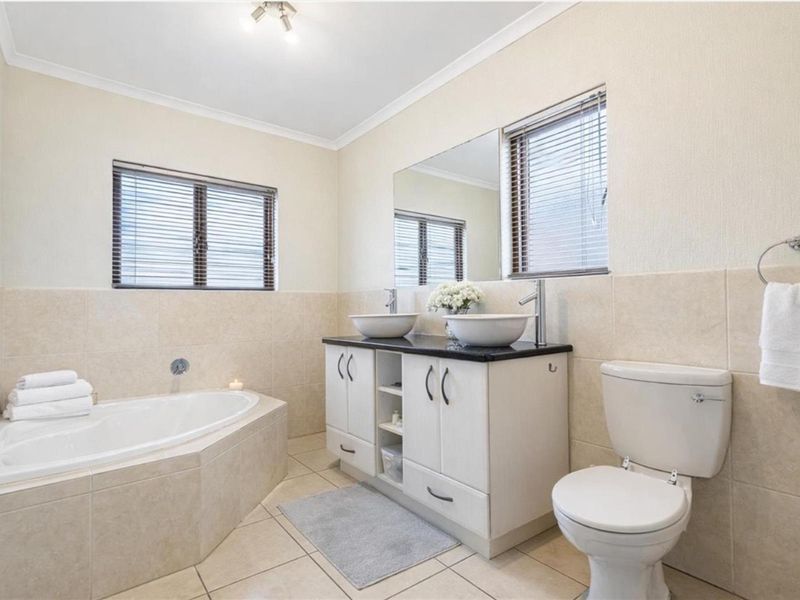 A well-maintained bathroom featuring a corner bathtub, a double vanity with vessel sinks, and neutral wall and floor tiling.