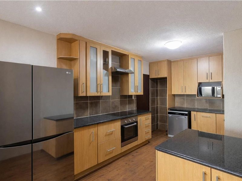 A functional kitchen featuring light wood cabinetry, dark granite countertops, a built-in oven, hob, extractor fan, and integrated microwave space.